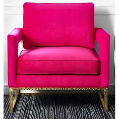 a pink chair sitting in front of a white wall with a black and gold striped rug