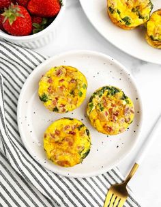 three breakfast muffins on a white plate with strawberries in the bowl next to them