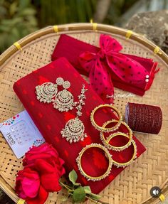 red and gold accessories are sitting on a woven tablecloth with a rose in the foreground