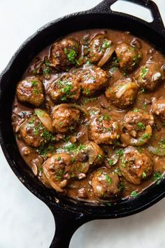 a skillet filled with meatballs and gravy on top of a table