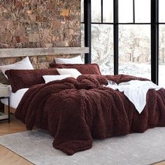 a bedroom with stone walls and flooring has a large bed covered in brown fluffy blankets