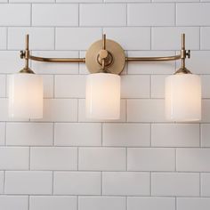 a bathroom light with three lights on the wall and white brick walls behind it,