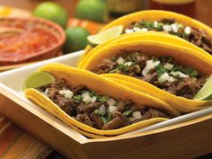 three tacos with meat, onions and cilantro on a plate next to salsa