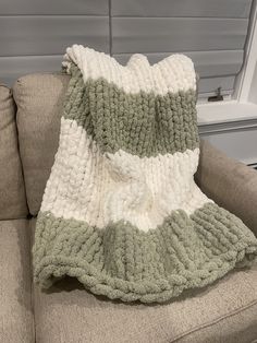 a green and white crocheted blanket sitting on top of a couch next to a window