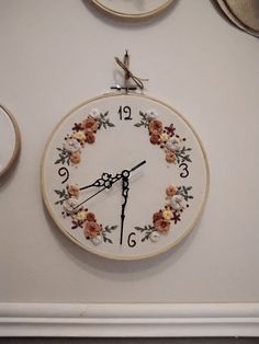 a white clock with flowers on it hanging from the wall