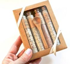 a hand holding a wooden spoon in a small box with spices inside and on it