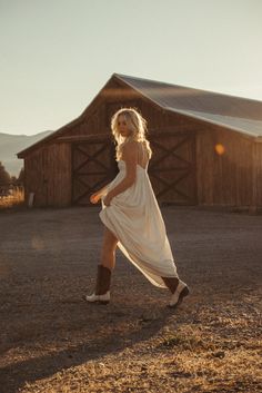 a woman in a white dress is walking by a barn