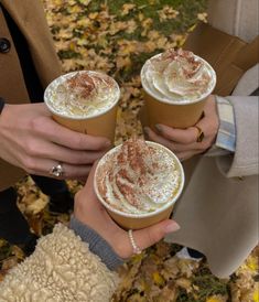 three people holding drinks in their hands with autumn leaves on the ground and trees behind them