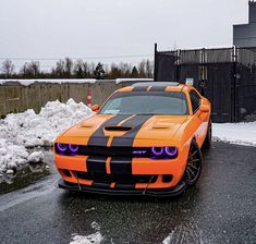 an orange and black car parked on the side of a road next to snow covered ground