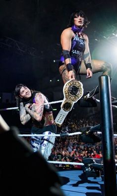 two wrestlers are in the middle of a match, one is holding up his belt