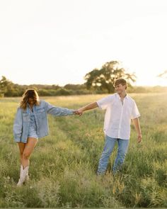 a man and woman holding hands walking through tall grass in an open field at sunset