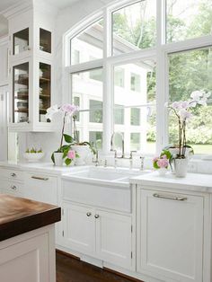 a white kitchen with lots of windows and flowers in vases on the sink counter