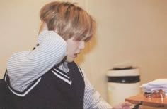 a young boy sitting at a desk with a cell phone to his ear and writing