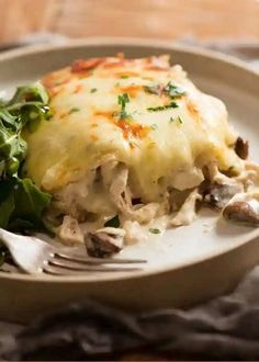 a white plate topped with lasagna covered in cheese and spinach next to a fork