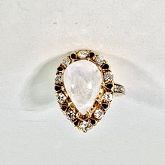 "Tear shaped moonstone ring, surrounded by 10 brilliant diamonds and enamelware 14 karat yellow gold. Could be a Victorian. Ring is 3/4\" long x 5/8\" wide Size: 6.5" White Pear-shaped Ring With Rose Cut Diamonds, White Pear-shaped Rose Cut Diamond Ring, White Moonstone Ring With Diamond Accents, White Moonstone Ring With Rose Cut Diamonds, Heirloom White Moonstone Ring With Rose Cut Diamonds, Luxury White Moonstone Ring With Diamond, Luxury White Diamond Moonstone Ring, White Multi-stone Moonstone Ring Fine Jewelry, White Cabochon Moonstone Ring In Fine Jewelry Style