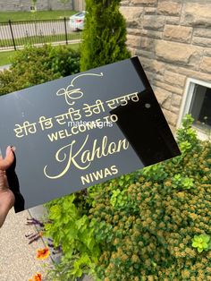 a person holding up a sign that says welcome to kalon niwas in front of a building