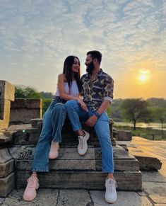 a man and woman sitting on steps with the sun setting in the background