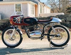 a red and black motorcycle parked in front of a brick wall with a house behind it