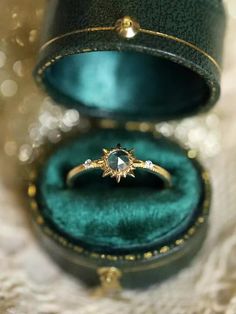 an open green velvet ring box with a white diamond in it and gold trimming around the edges