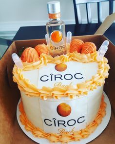 a cake in a box with orange icing on it and a bottle of ciroc