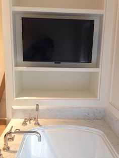 a white sink sitting under a flat screen tv mounted on a wall in a bathroom