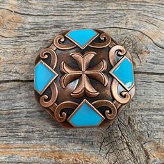 a blue and brown brooch sitting on top of a wooden table next to a piece of wood