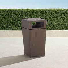 a brown trash can sitting in front of a hedge