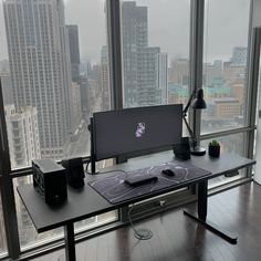 a desk with a computer on top of it in front of a window overlooking the city