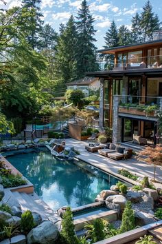 an outdoor swimming pool surrounded by trees and rocks in front of a large house with lots of windows