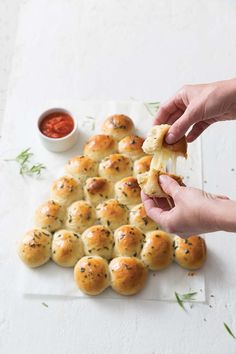 a person holding a piece of bread in front of some rolls on a white surface