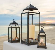 two lanterns with seashells and candles on the beach