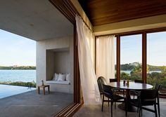 a table and chairs in front of an open window overlooking the water with curtains on it