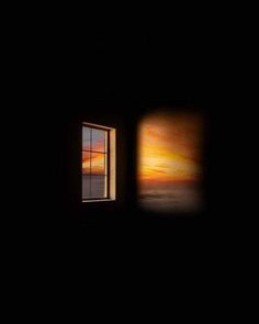 an open window in a dark room with the sun going down and some clouds coming out