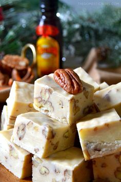 several pieces of fudge with pecans on the side and a bottle of maple syrup in the background