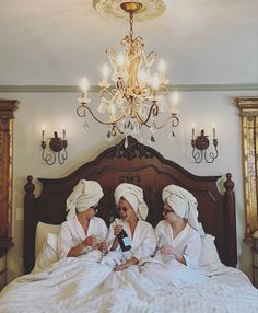 three women in white robes are sitting on a bed and one is holding a bottle