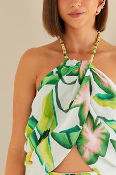 Embrace the tropical vibe with the Summer Foliage Off White Croped Top by FARM Rio. This halter neckline top features a vibrant leafy pattern, evoking the lush landscapes of Brazil. The delicate ruffles and eyelet fabric add a touch of femininity to the piece, while the cropped silhouette keeps it modern and fresh. Perfect for a summer day out, this top will bring a playful and stylish flair to your wardrobe. Composition 55% LINEN 45% VISCOSE Care Instructions MACHINE WASH GENTLE CYCLE, DO NOT B Tropical Print Sleeveless Halter Top, Sleeveless Tropical Print Halter Top For Vacation, Summer Tropical Print Halter Top Beachwear, Summer Tropical Print Halter Top For Beachwear, Summer Beachwear Halter Top With Tropical Print, Tropical Summer Halter Neck Top, Tropical Halter Neck Top For Summer, Spring Vacation Tropical Print Halter Top, Summer Tropical Print Sleeveless Halter Top