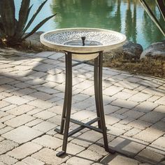 an outdoor table with a bird bath on it's side in front of a pond