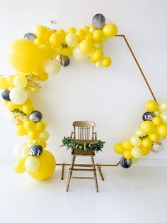 a chair sitting in front of a bunch of yellow and white balloons hanging from the ceiling