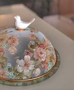 a white bird sitting on top of a floral covered dish with mesh covering over it