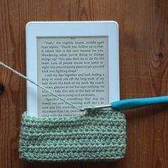 an electronic device with a knitted book cover next to it and a blue crochet hook