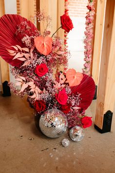 a vase filled with red flowers sitting on top of a floor next to a mirror ball