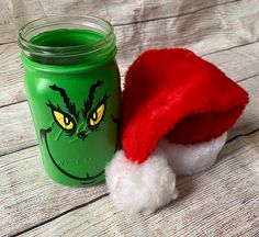 a green mason jar with a red santa hat next to it on a wooden table