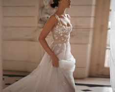 a woman in a wedding dress is standing near a window and looking off into the distance