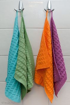 three colorful towels hanging from hooks in a bathroom