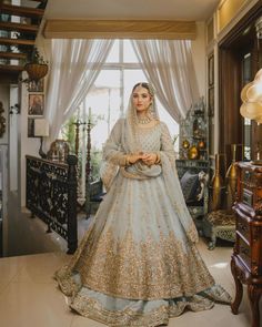 a woman in a white and gold bridal gown posing for the camera with her hands on her hips