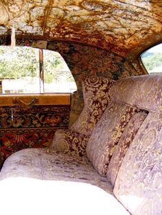 the inside of an old car that has been decorated with decorative fabric and pillows on it