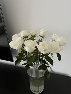 white roses are in a clear vase on a black countertop next to a mirror