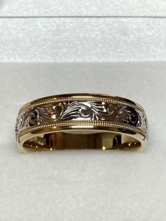 a gold wedding band with an intricate design on the inside and outside, sitting in a white box