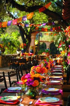 a long table set with colorful plates and place settings for an outdoor dinner or party