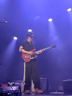 a man standing on top of a stage with a guitar in his hand and lights behind him